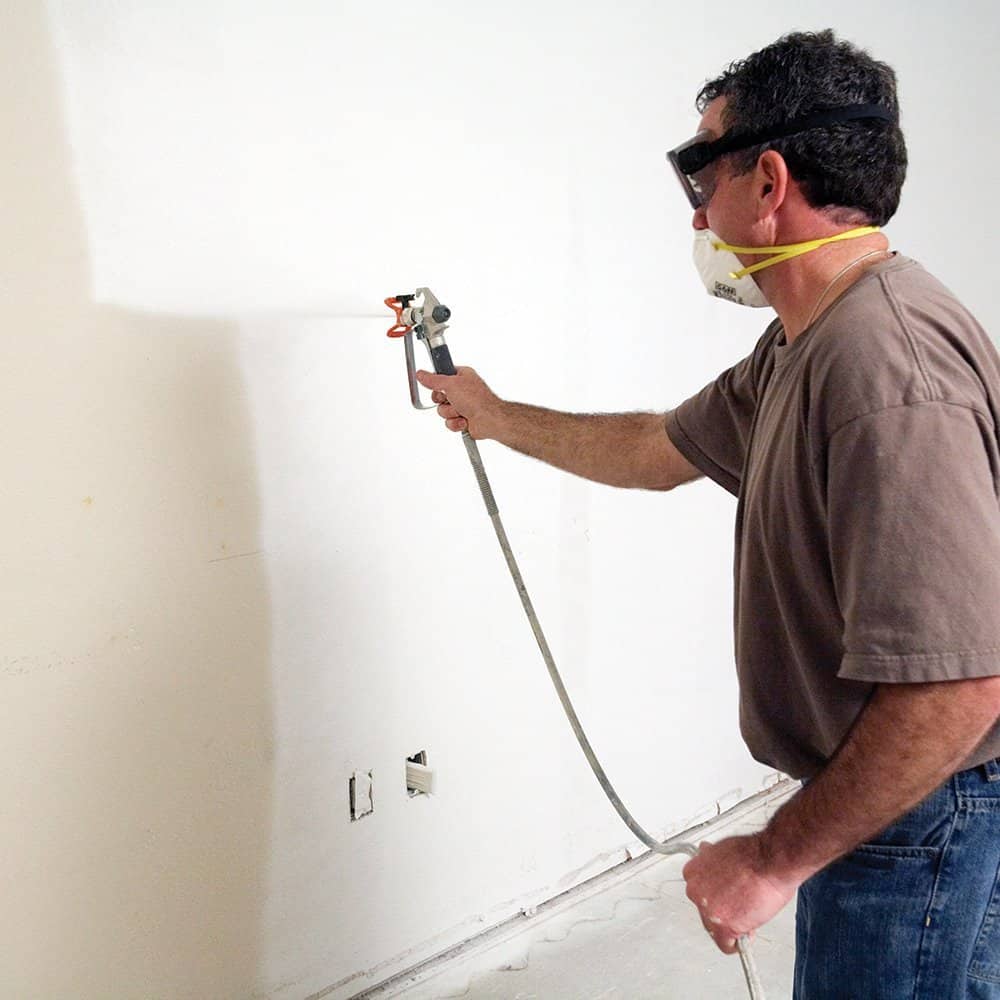 Photograph of a man using an airless paint sprayer machine